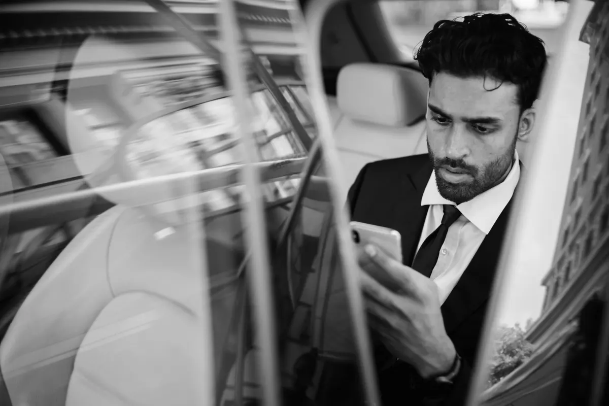 Businessman checking his phone in the back of a chauffeur-driven car